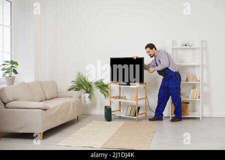 Young professional male TV technician installs and connects new TV in customer's house. Stock Photo