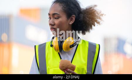 smile African american woman foreman worker  or woman maintenance engineer in reflective vest safety jacket sits down on old truck for relaxing, eats Stock Photo