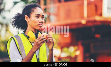 smile African american woman foreman worker  or woman maintenance engineer in reflective vest safety jacket sits down on old truck for relaxing, eats Stock Photo