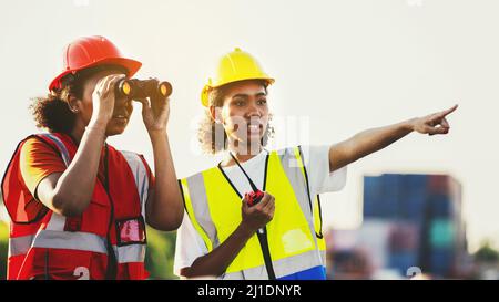 Woman foreman or engineer using binoculars and partner pointing at problem focus cargo container tank at the warehouse container logistic transportati Stock Photo