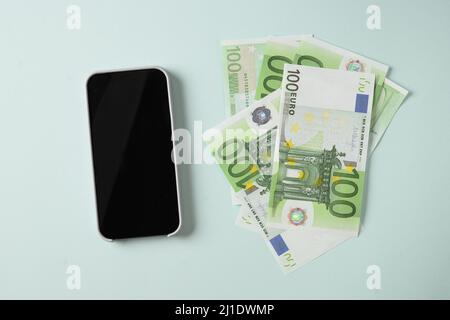 European money in banknotes of 100 euros bills and smartphone screen on blue background. Copy space. View from above. Concept online pay and earnings. Stock Photo