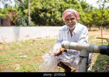 Happy Indian farmer after seeing water on borewell pipe at farmland - cocnept of happiness, poverty and water for agricultural works Stock Photo