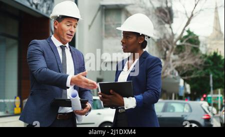 Developing the city for the better together. Shot of two businesspeople wearing hard hats having a discussion outdoors in the city. Stock Photo