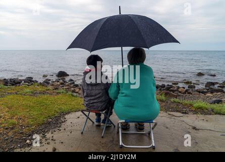 Grandmother and grandson have a nice conversation sitting under an umbrella on the seashore Stock Photo