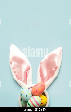 Happy Easter. Colored easter painted eggs on white rabbit ears with copy space over blue background Stock Photo
