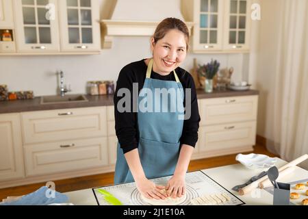 Young asian woman cooking pastry from dough in modern home kitchen interior. Stock Photo