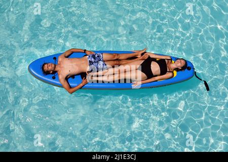 29.07.2021, Italy, Viterbo, Bolsena - young couple lying in a swimming pool on a SUP board. 00S210729D197CAROEX.JPG [MODEL RELEASE: NO, PROPERTY RELEA Stock Photo