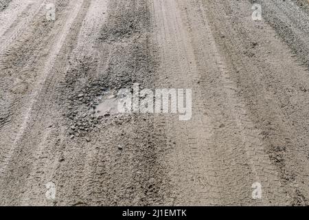 crumbling dirt road without asphalt pavement, made of clay and dirt with rubble, with pits and potholes filled with water, puddles wet after rain Stock Photo
