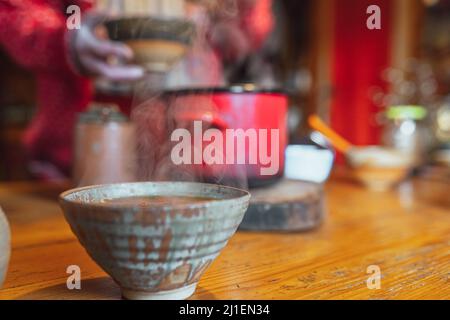 man in casual rustic clothes pours soup from large authentic pot into ceramic plate with ladle Stock Photo