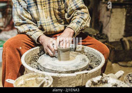 Muscular hands of middle-aged man, potter, soiled in clay, form pottery from clay on potter's wheel Stock Photo
