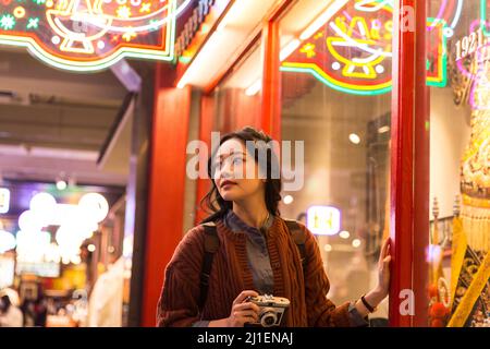 Beautiful young Chinese female tourist looking for exhibits outside show window - stock photo Stock Photo