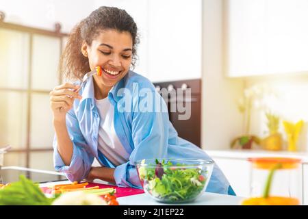 Young woman in the home kitchen eating a genuine salad with fresh vegetables Stock Photo