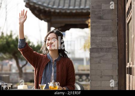 Chinese white-collar female greeting friend and enjoying afternoon tea in sidewalk cafe - stock photo Stock Photo