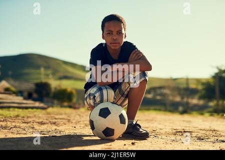 He loves the beautiful game. Portrait of a little boy crouching on a field outside with a soccer ball. Stock Photo