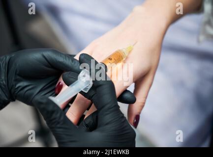 Close up of beautician in black rubber gloves doing injection in hand for anti-aging skin. Concept of procedure improvement skin with special preparation in professional beauty salon. Stock Photo