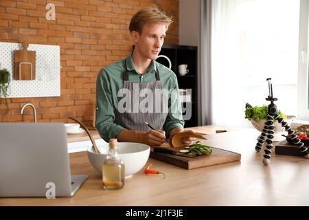 Young man making notes from cooking video tutorial in kitchen Stock Photo