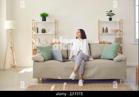 Happy beautiful senior woman sitting on sofa at home resting after working on laptop. Stock Photo
