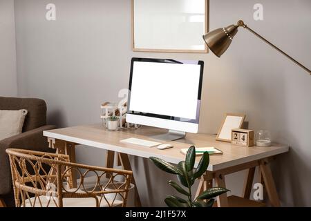 Comfortable workplace with modern computer and glowing lamp near grey wall in room Stock Photo