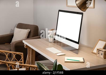 Comfortable workplace with modern computer and glowing lamp near grey wall in room Stock Photo