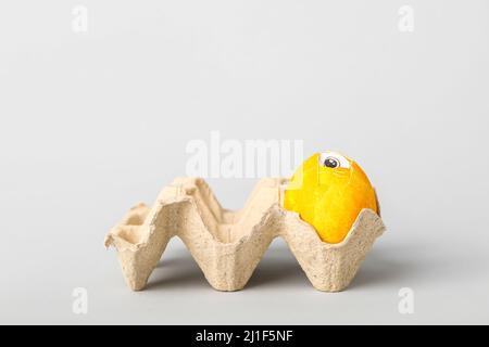 Holder with creative painted egg with drawn eye visible through broken shell on light background Stock Photo