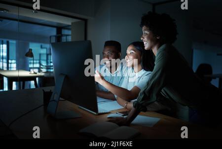 Those who keep at it hold the keys to success. Shot of a group of young businesspeople using a computer together during a late night at work. Stock Photo