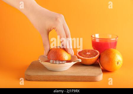Woman squeezing fresh orange on orange background Stock Photo