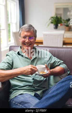 Portrait of smiling caucasian senior man having coffee while sitting on sofa at home Stock Photo