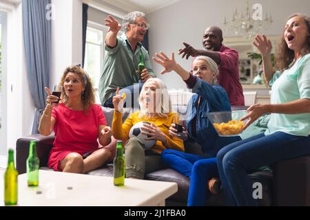 Shocked multiracial senior friends watching soccer match on tv at home Stock Photo