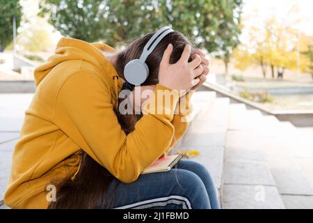 Sad teenage girl in headphones will cover her face with her hands, a place for text Stock Photo