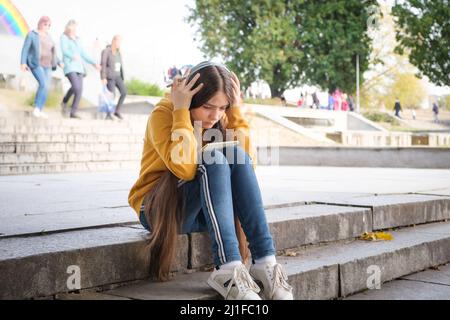 A sad teenage girl sits on the stairs and covers her head with her hands Stock Photo