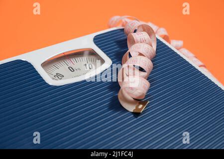 Floor blue scales and centimeter measuring tape on an orange background, top view. The concept of weight loss and weight control Stock Photo