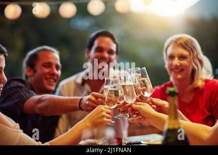 Good times are for celebrating with friends. Shot of a group of happy young friends toasting with champagne at a backyard dinner party. Stock Photo