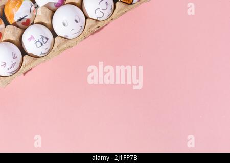 White eggs with different painted faces placed in the corner of the image on a pink background. Minimal concept. Top view, copy space. Stock Photo