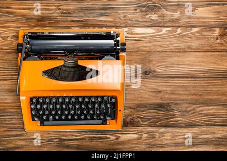 top view of orange typewriter on brown wooden surface Stock Photo