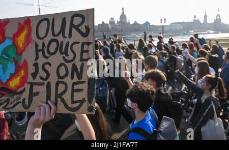 Dresden, Germany. 25th Mar, 2022. Participants of a demonstration of Fridays for Future walk along the Carola Bridge in front of the Old Town. One participant carries a sign with the inscription 'Our House is on Fire'. Around the world and also in many German cities, climate protests are taking place this Friday under the slogan #PeopleNotProfit. The organization Fridays for Future is calling for an end to dependence on fossil fuels. Credit: Robert Michael/DPA-Zentralbild/dpa/Alamy Live News Stock Photo