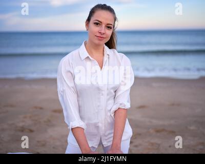 A young chiromassage therapist dressed in white standing on a beach in Valencia with the sea in the background. Stock Photo