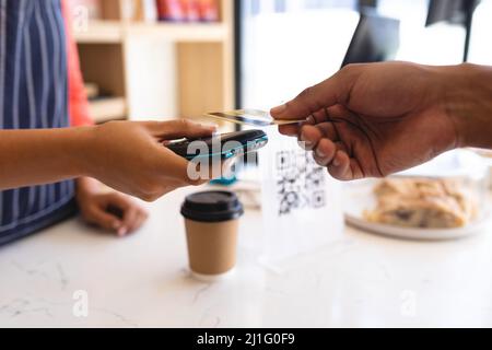 Cropped hand african american male customer paying through credit card at counter in coffee shop. unaltered, cafe culture, technology, occupation and Stock Photo