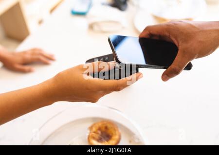 Cropped hands of multiracial customer and owner doing contactless payment through smartphone at cafe. unaltered, cafe culture, technology, occupation Stock Photo