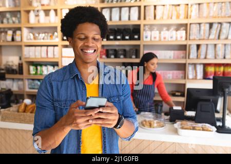 Smiling young african american male customer using smartphone against owner at coffee shop. unaltered, cafe culture, people, technology and lifestyle Stock Photo