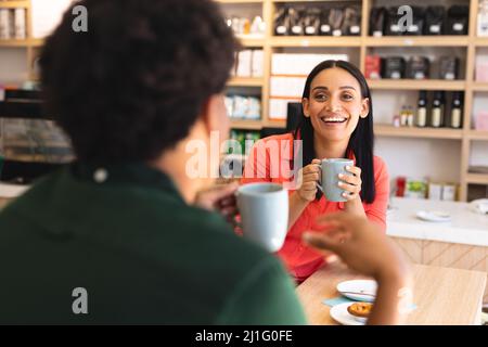 Happy young biracial couple talking while enjoying coffee sitting at tablet in cafe. unaltered, cafe culture, people, love and lifestyle concept. Stock Photo