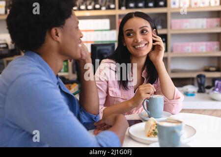 Happy multiracial young couple sitting with coffee and snack at table in coffee shop. unaltered, cafe culture, people, love and lifestyle concept. Stock Photo