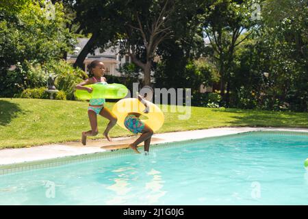 African american siblings jumping with inflatable ring in swimming pool on sunny day Stock Photo