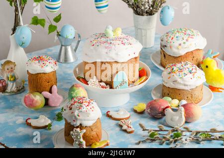 Easter cakes and eggs on a festive Easter table with willow and a figurine of a rabbit on a blue background. Stock Photo