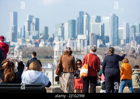 London, UK. 25th Mar, 2022. UK Weather : People enjoy the view of Canary Wharf and the warm conditions in Greenwich Park as the temperature is forecast to rise to nearly 20C on a fine Spring afternoon. On 27 March, the UK will move to British summer time, with clocks going forward one hour. Credit: Stephen Chung/Alamy Live News Stock Photo