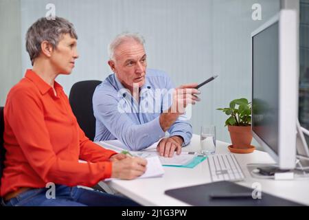 Highlighting the stages of the project. Shot of two mature business colleagues discussing work at a desktop computer. Stock Photo
