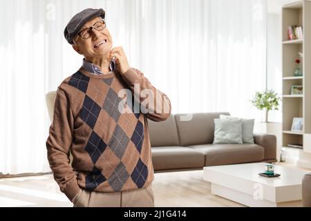Elderly man itching his neck and standing inside a living room Stock Photo