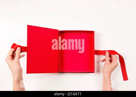 Female hands opening empty red elegant luxury box with ribbon. Mockup present gift box on white table background. Top view Stock Photo