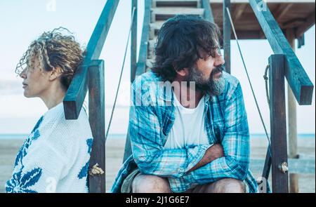 Serious pensive adult man thinking of relationships problems sitting outdoor with offended wife, conflicts in marriage, upset couple after fight dispu Stock Photo