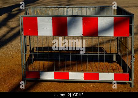 small hoarding (barrier fence) in red and white stripes at a playground in the sunshine Stock Photo