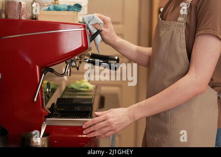 Medium section side view shot of unrecognizable female cafe worker wearing apron cleaning modern espresso coffee machine Stock Photo